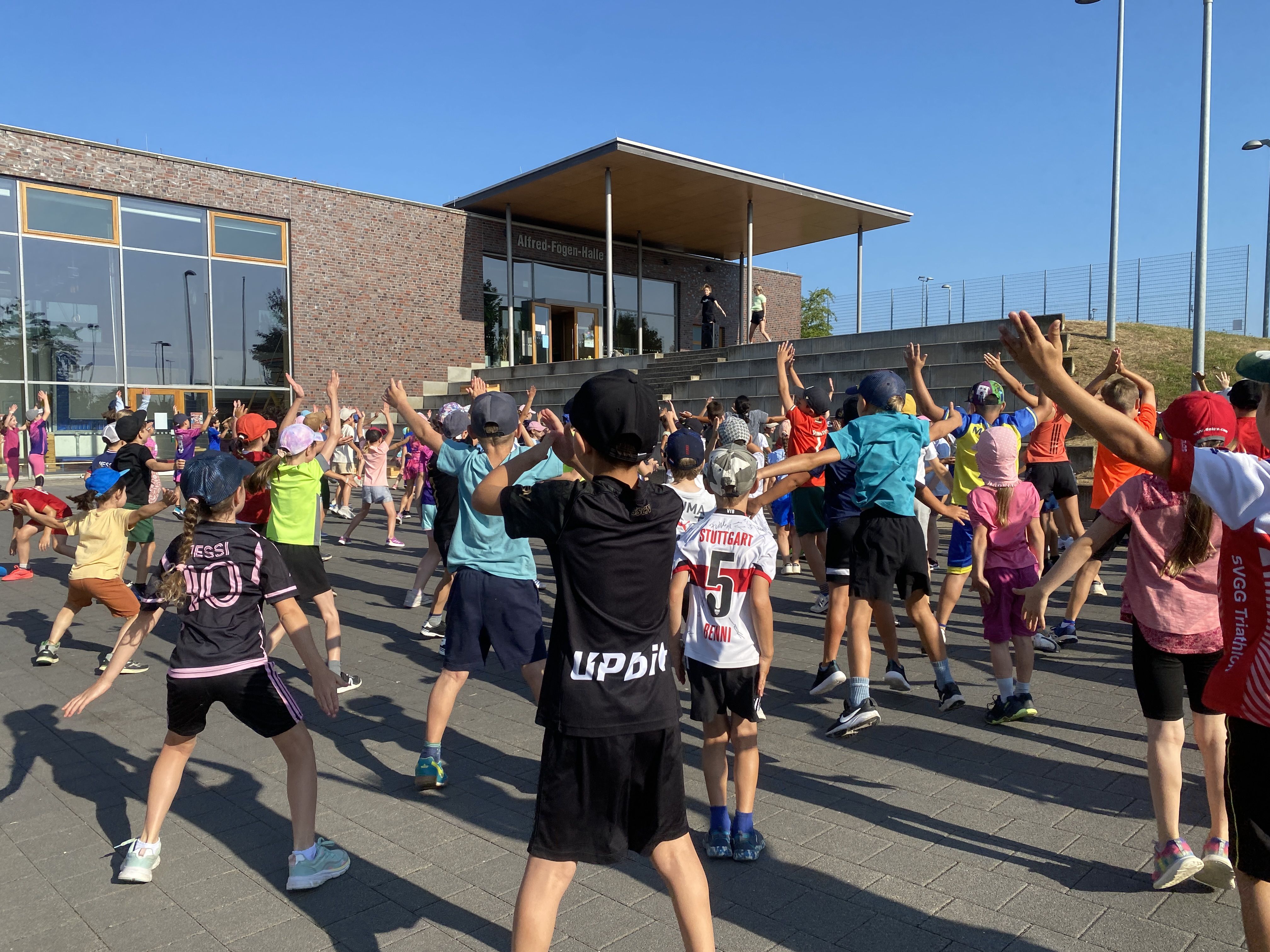 Viele Kinder machen sich auf einem großen Platz mit Hampelmännern warm.