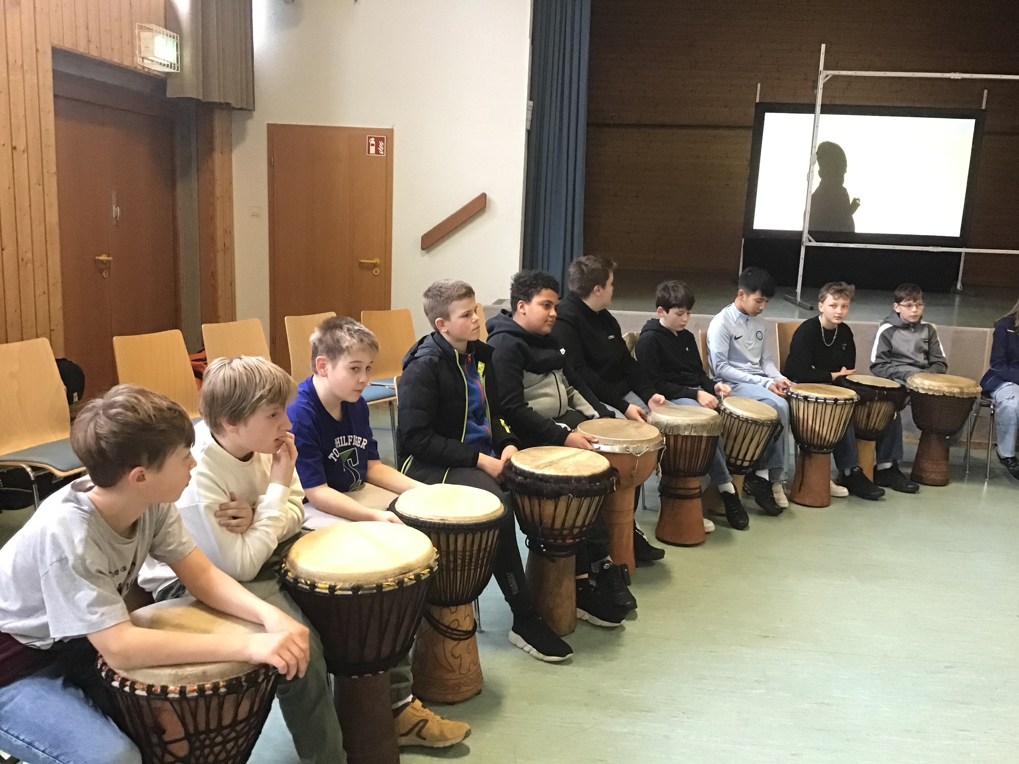 Eine Gruppe Kinder sitzt im Halbkreis vor Trommeln. 