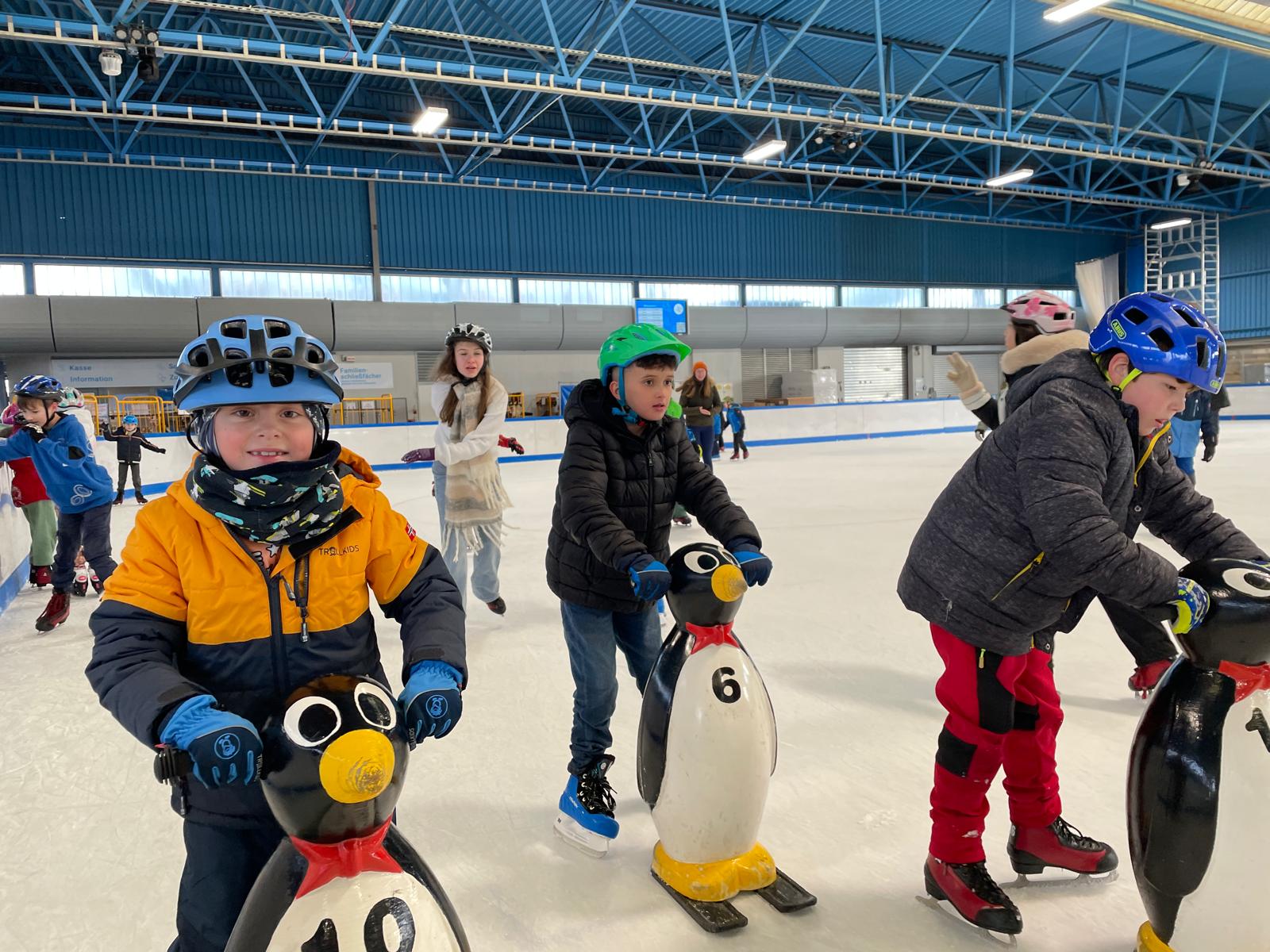 Bildbeschreibung: Drei Kinder st&uuml;tzen sich auf Holzpinguine, um auf dem Eis nicht zu fallen.