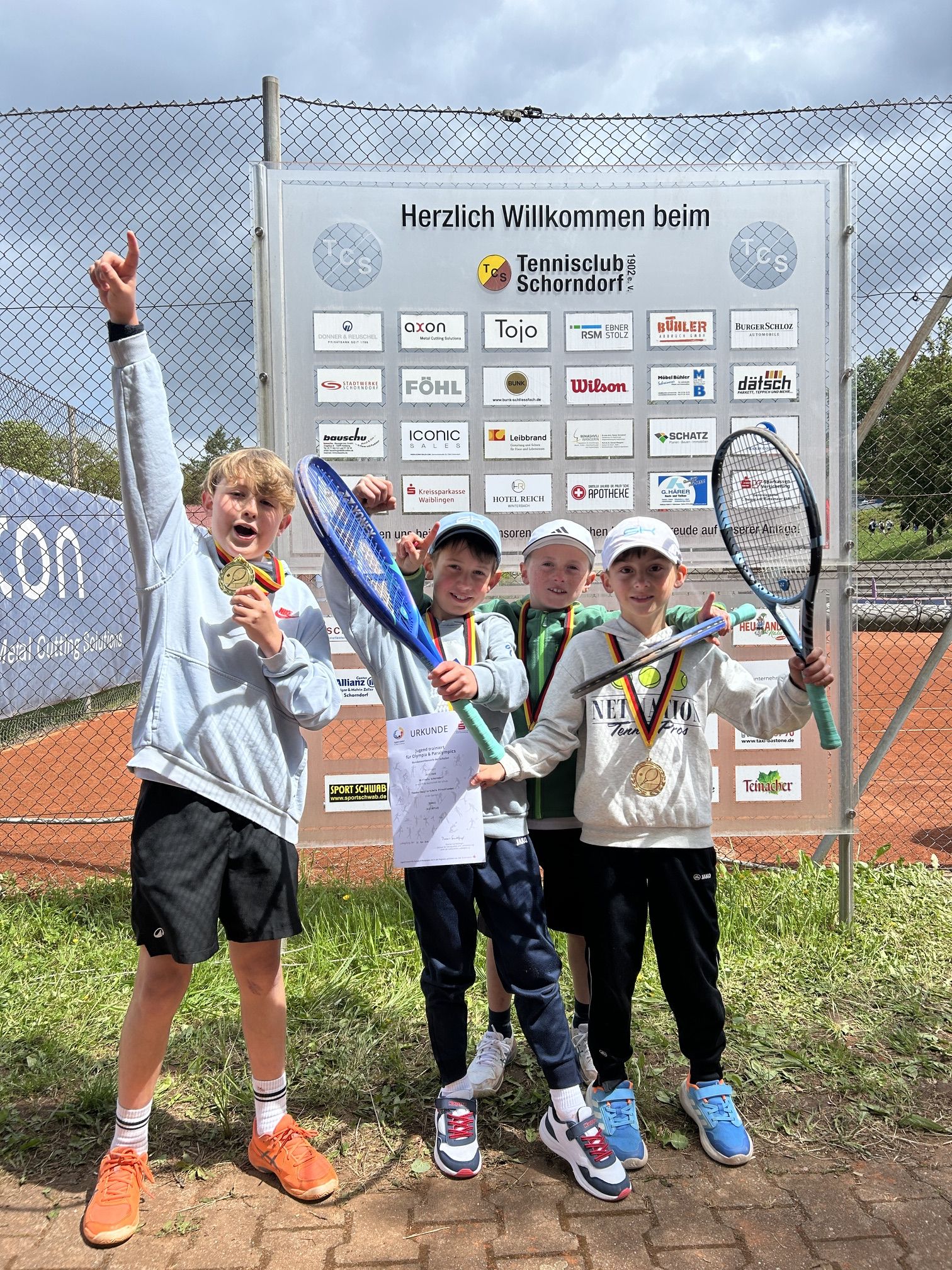 Vier Jungen halten ihre Medaillen und Tennisschläger in die Luft.
