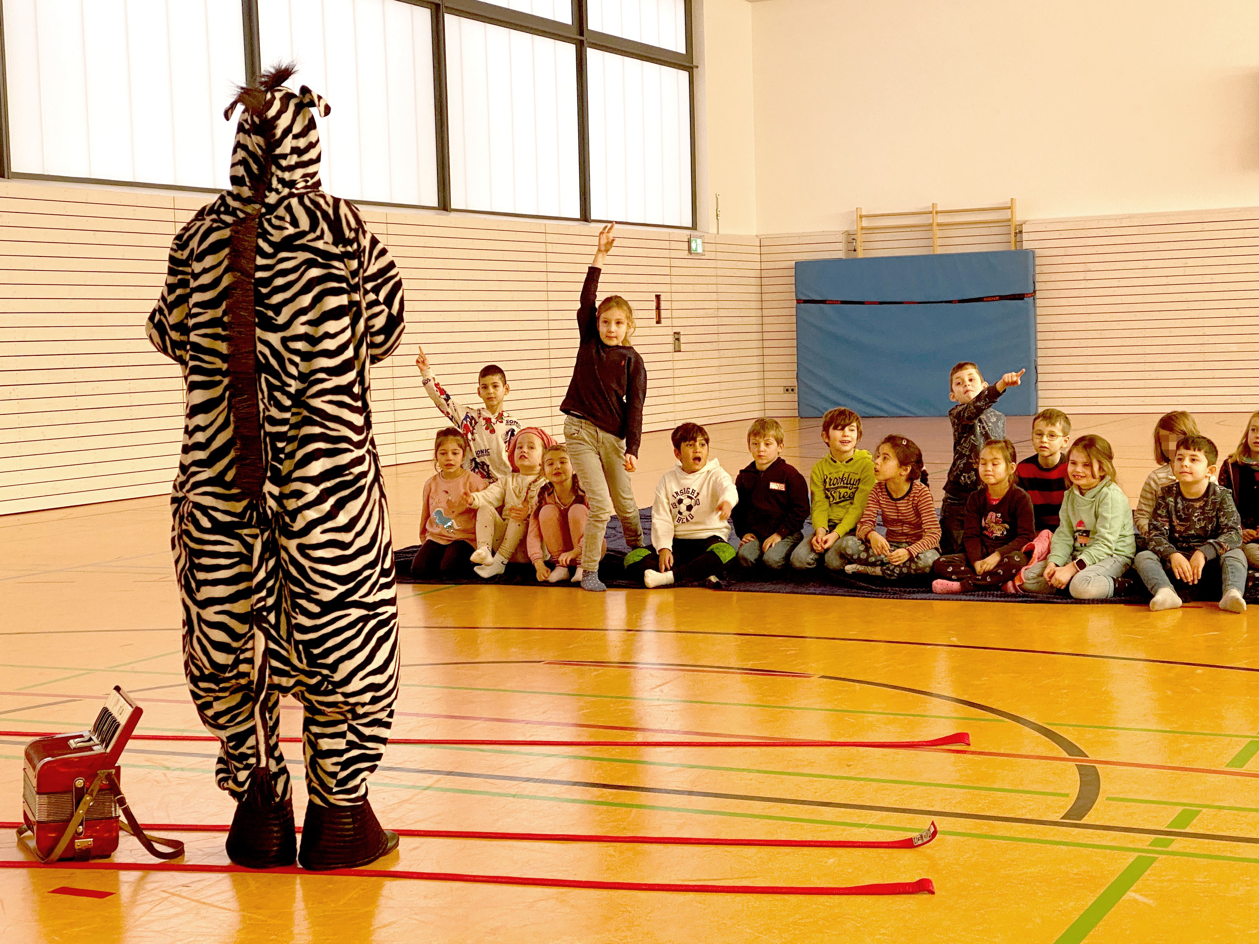Eine, als Zebra verkleidete Schauspielerin steht vor Kindern, die sich melden.