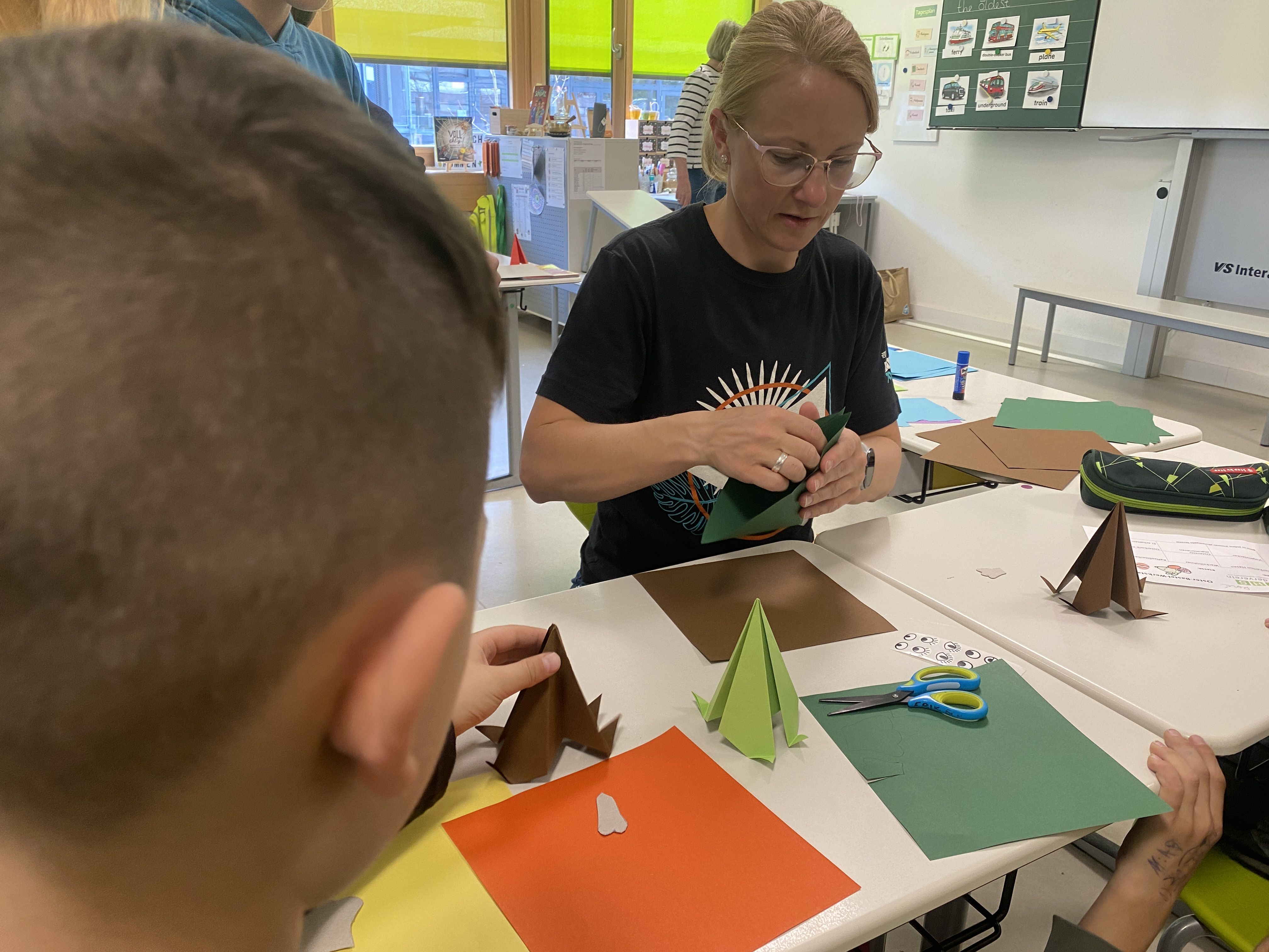 Eine Frau zeigt Kindern, wie ein Papier gefaltet wird.