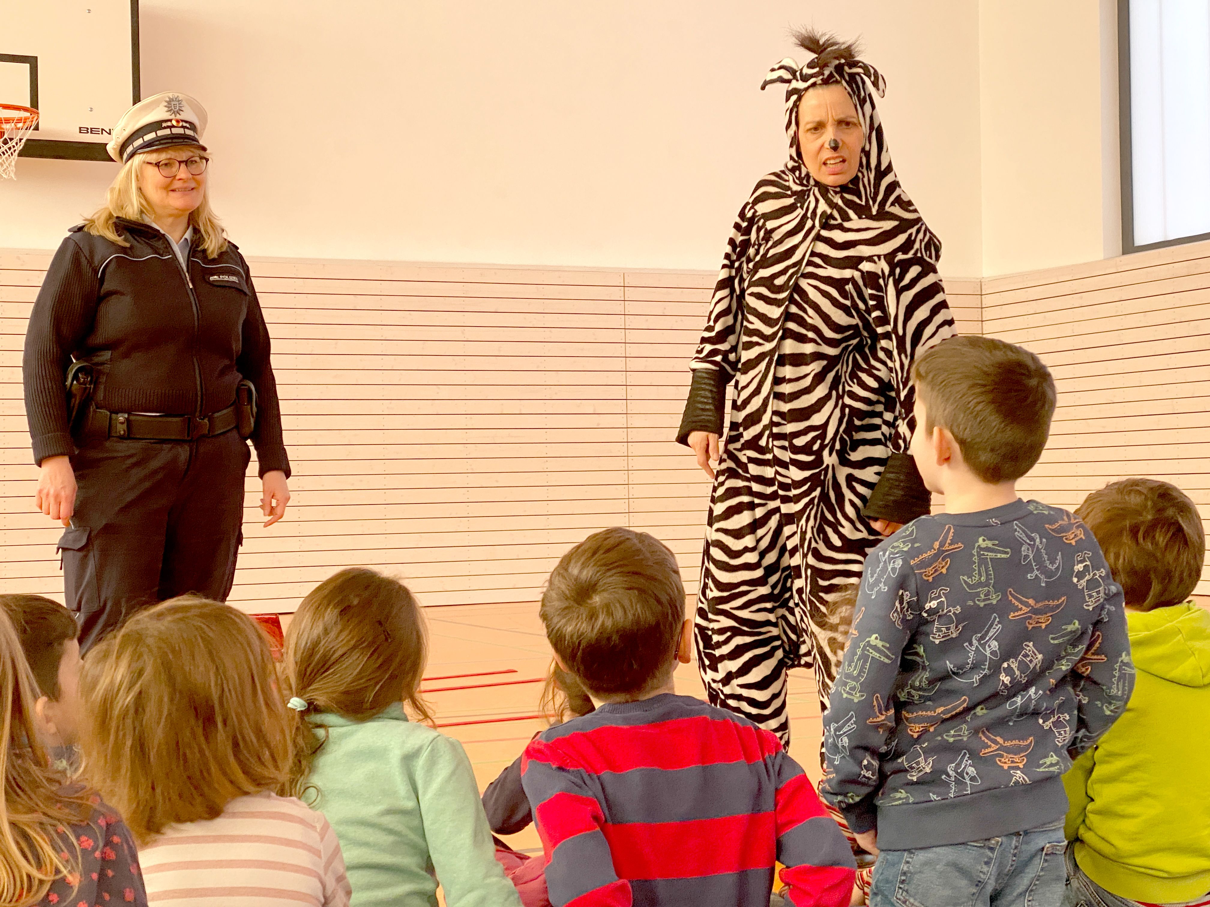 Eine Polizistin und eine, als Zebra verkleidete Schauspielerin stehen vor Publikum.