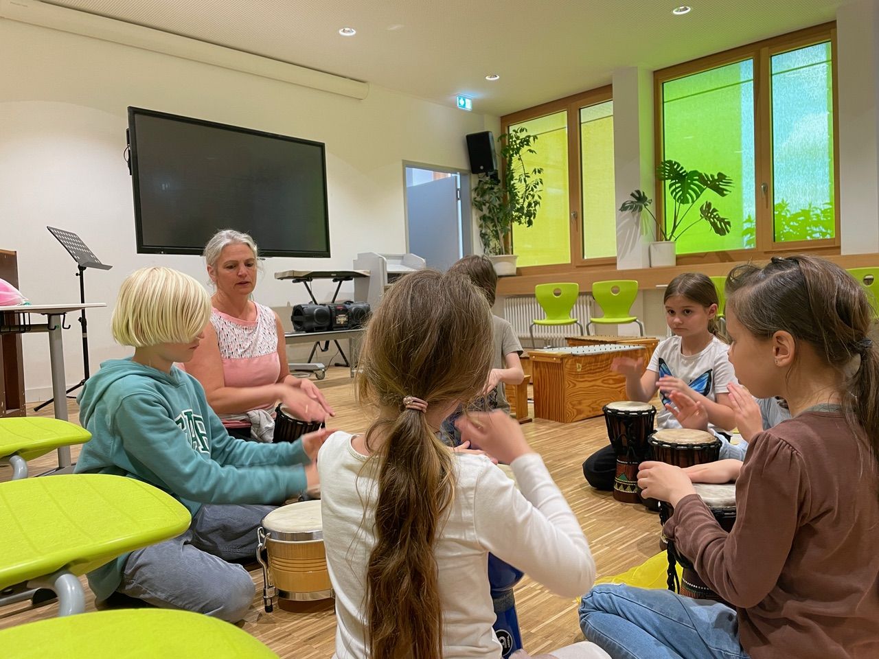 Mehrere Kinder sitzen im Kreis und spielen auf Trommeln.