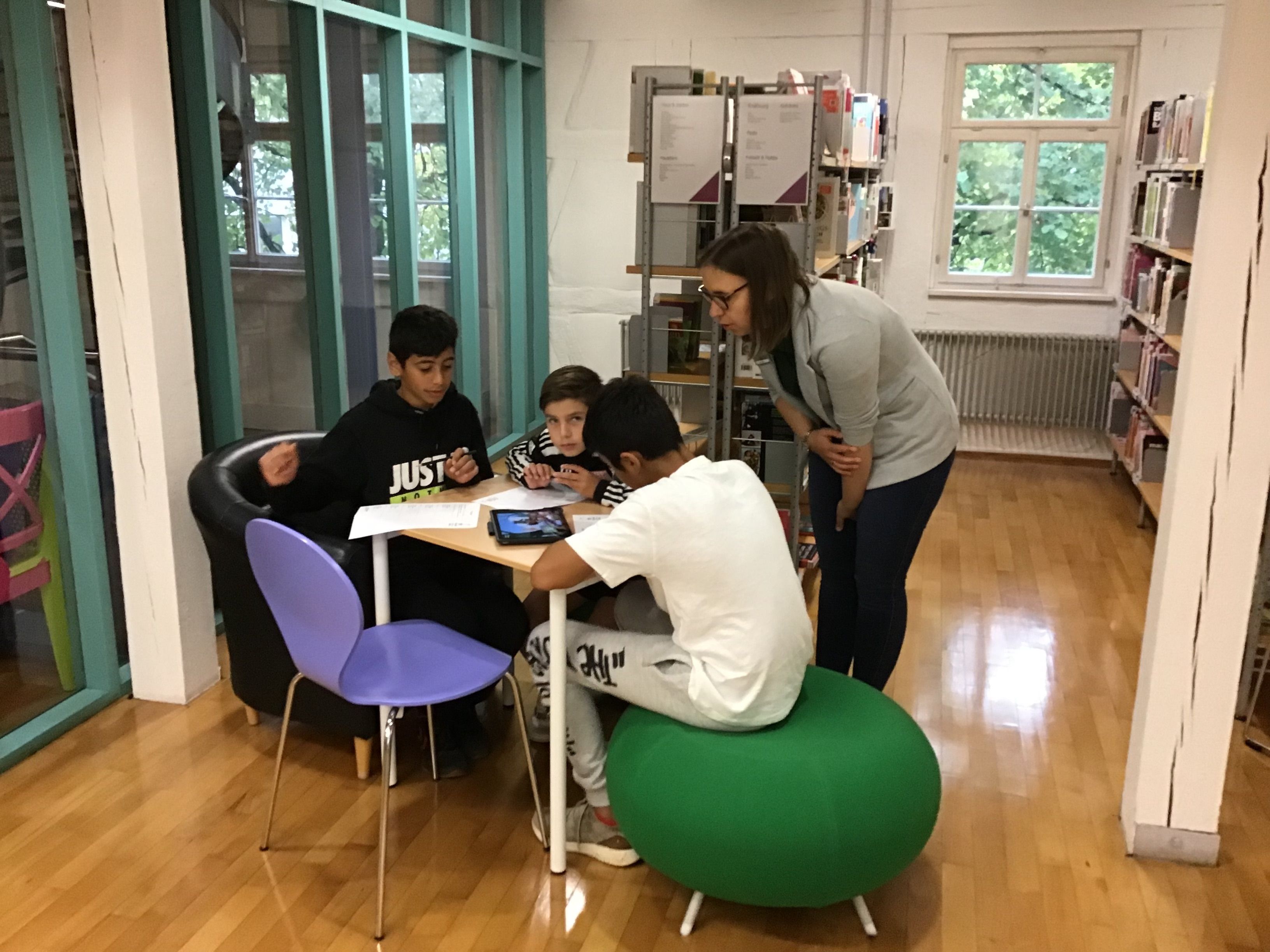 Eine Jungsgruppe und eine Mitarbeiterin der Bibliothek beim prüfen von Apps