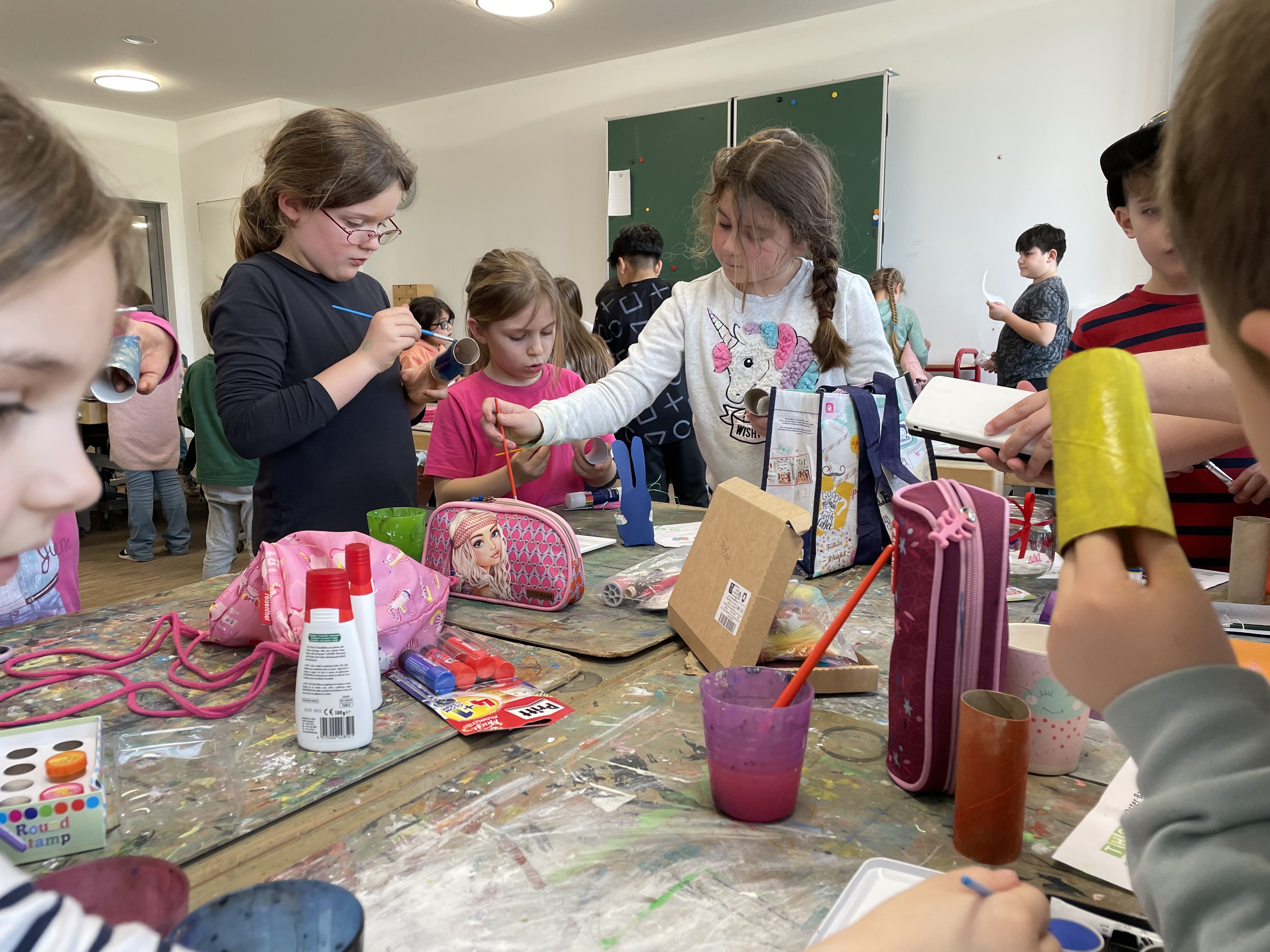 Kinder stehen um eine Werkbank herum und basteln. Auf dem Tisch liegen Bastelutensilien.