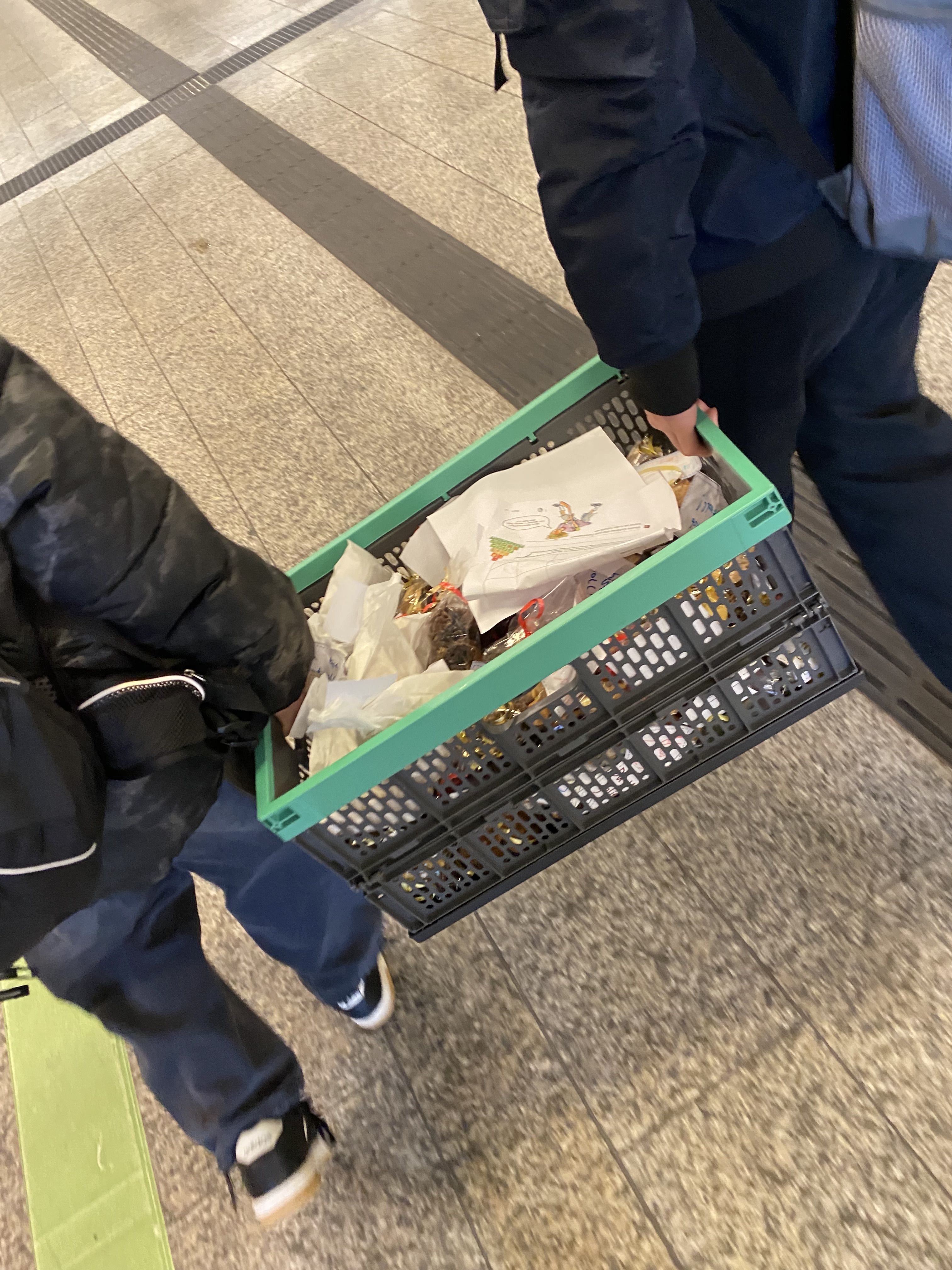 Zwei Schüler tragen eine mit Plätzchen gefüllte Klappbox.