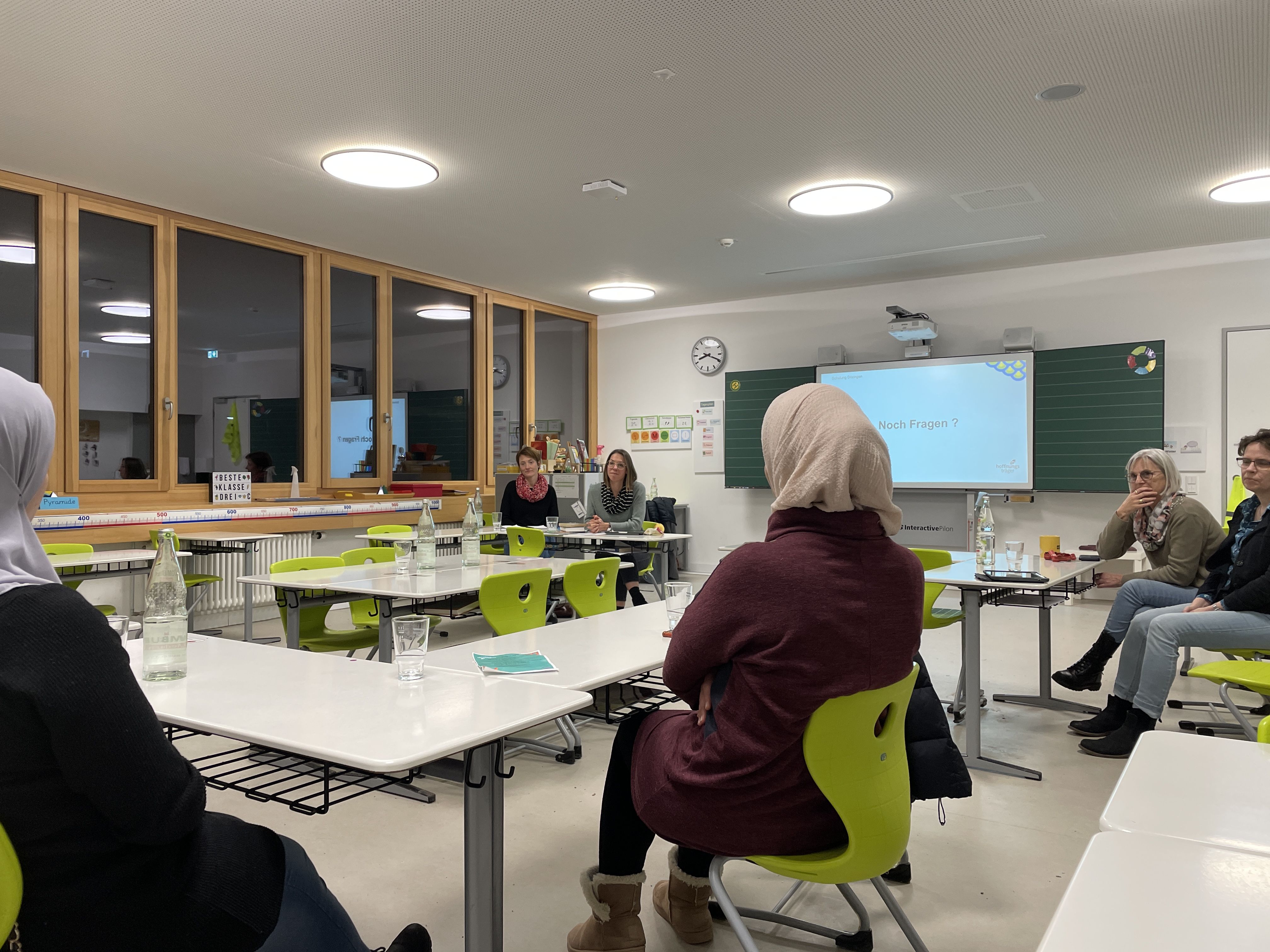 Bildbeschreibung: Zuhörende sitzen an Tischen in einem Klassenzimmer.