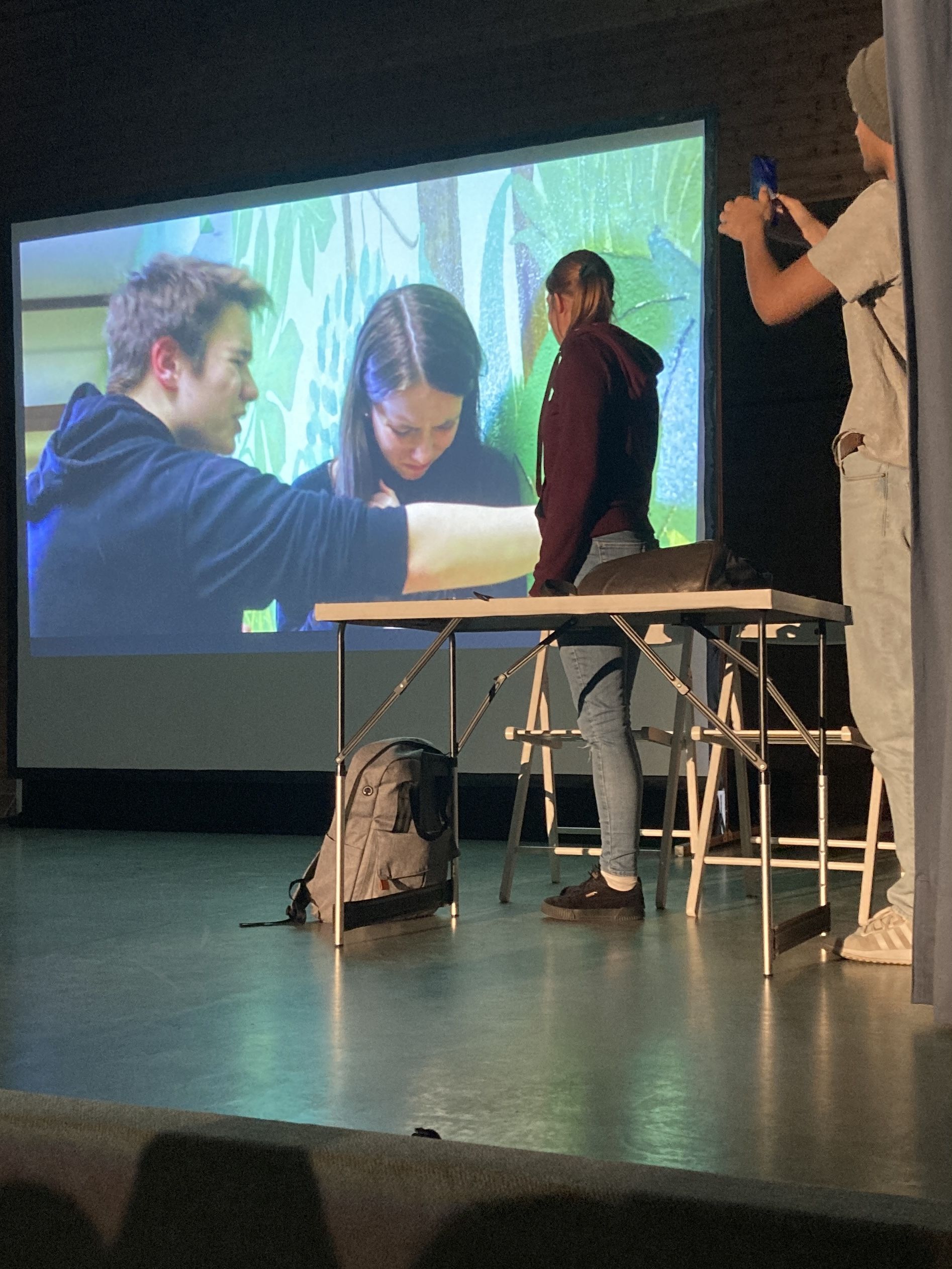 zwei Schauspieler auf der Bühne, im Hintergrund ein Video